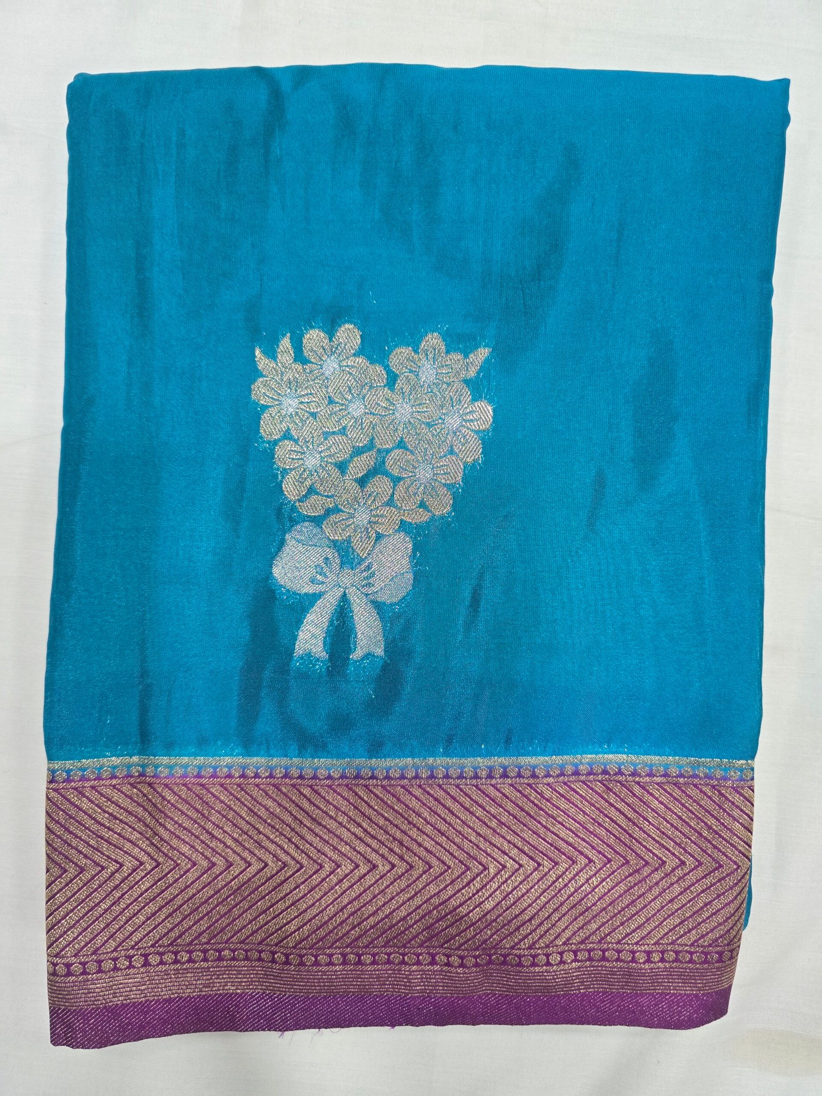 Soft Silk Saree showing a blue body with a gold floral motif and purple border.